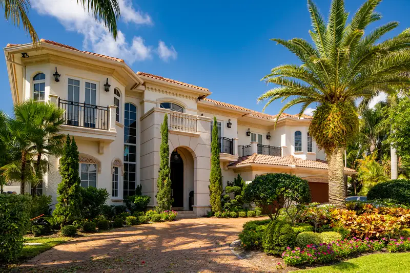Multi-story luxury estate showcasing dense, colorful garden landscaping. Multi-story luxury estate showcasing dense, colorful garden landscaping.