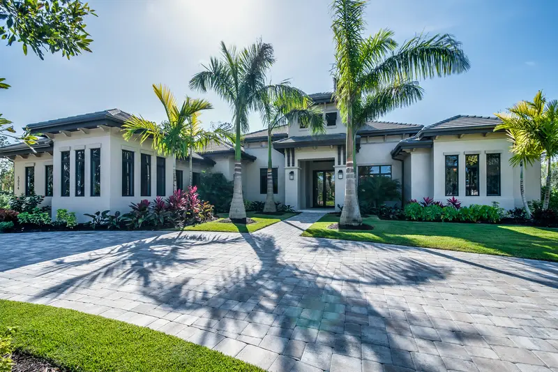 Luxury estate home featuring palm trees and a spacious paved stone driveway. Luxury estate home featuring palm trees and a spacious paved stone driveway.