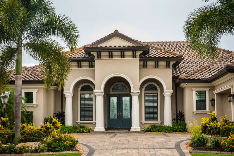 Luxury home with palm trees, paved driveway, and colorful landscaping Luxury home with palm trees, paved driveway, and colorful landscaping