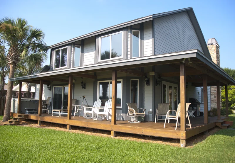 Two-story house featuring a large wooden deck porch surrounded by a green lawn. Two-story house featuring a large wooden deck porch surrounded by a green lawn.