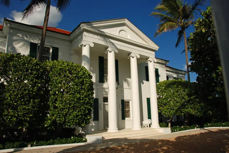 White plantation style mansion with neat hedge trimming and landscaping